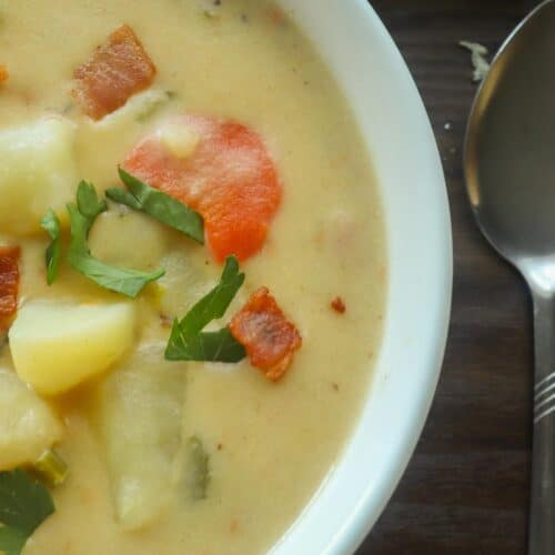 a plate of potato soup with a spoon and piece of bread on the side.