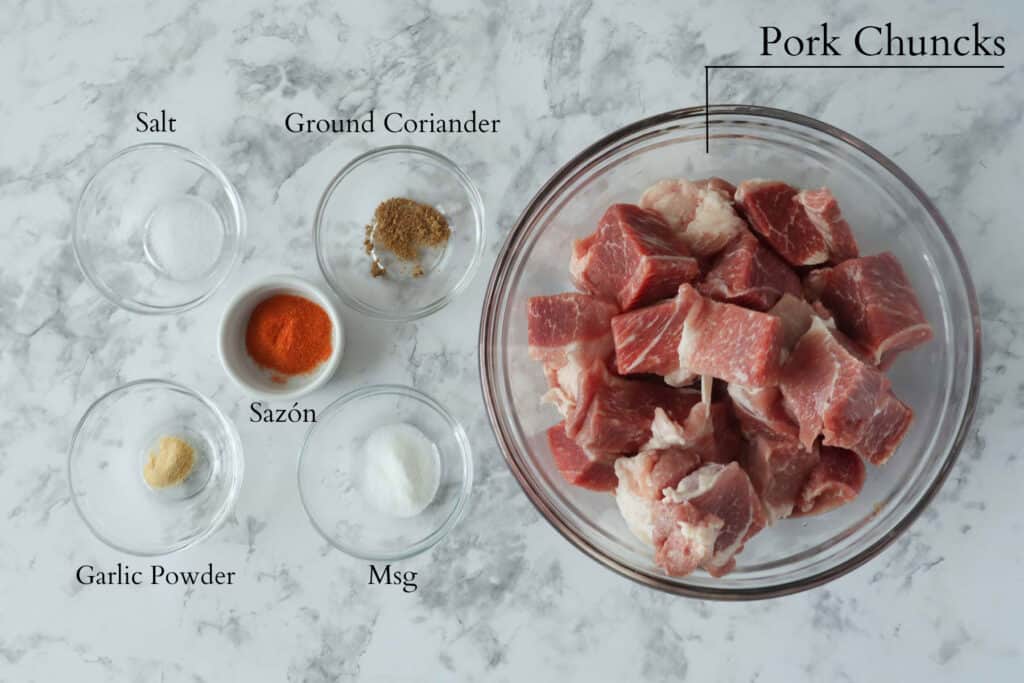 Ingredients to make carne frita- fired pork which includes pork chunks, ground coriander, salt, sazon seasoning, msg, and garlic powder.