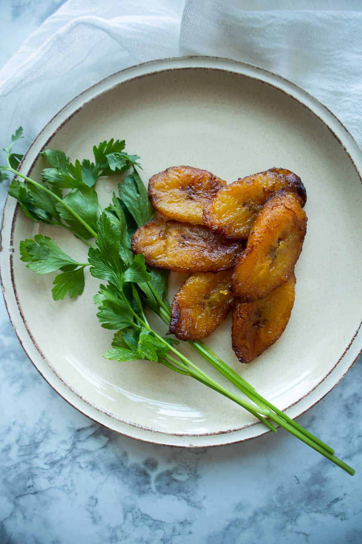 a plate with fried amarillos or fried plantains with parsley on a stem.