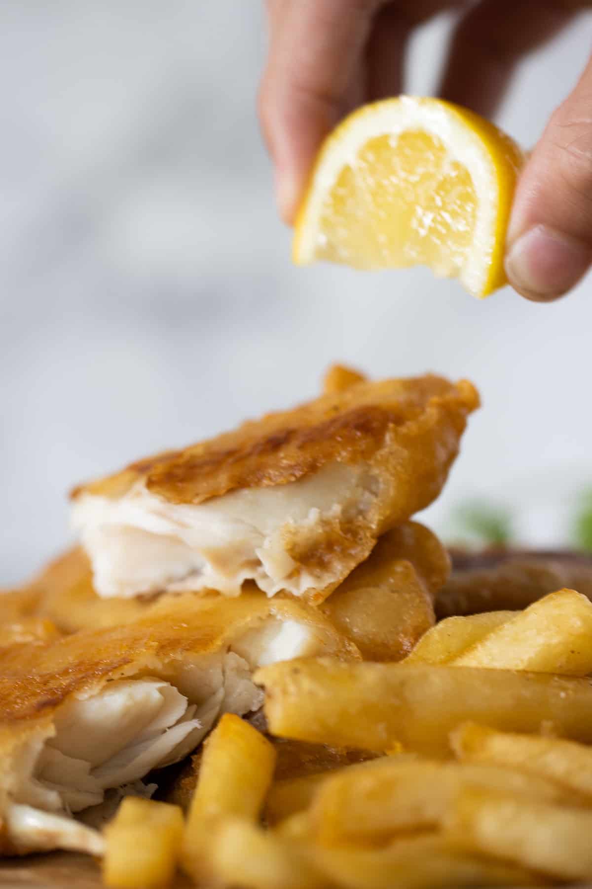 fried tilapia with french fries and a hand squeezing a lemon on top.