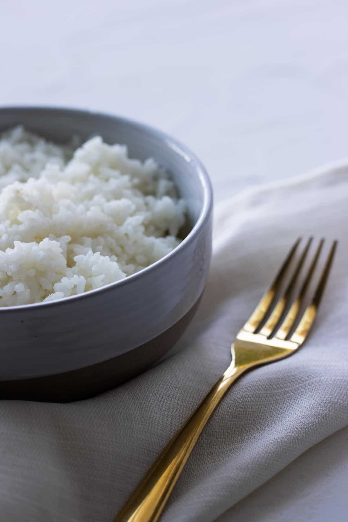 close up of a bowl of white rice and a golden fork next to it.
