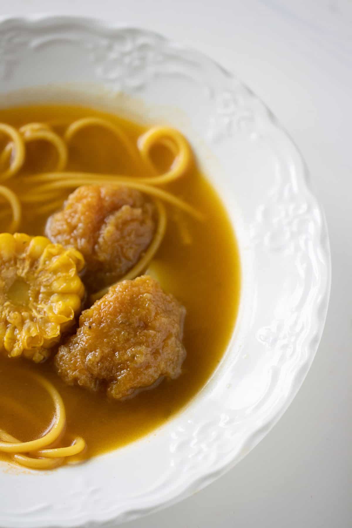 a white bowl with soups and plantain balls.