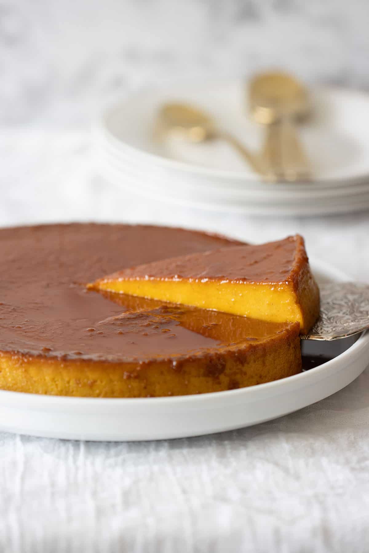 a piece of flan de calabaza-pumpkin flan being pick up with a cake server with plates and spoons in the background.