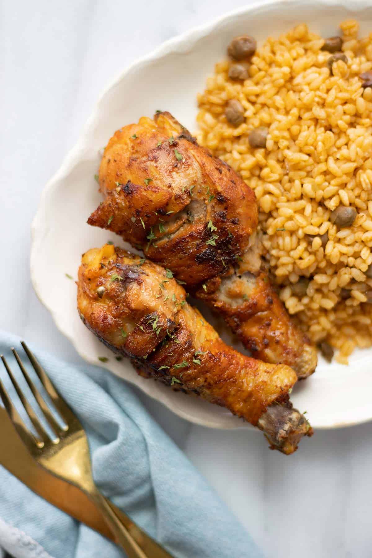 2 muslos de pollo con arroz con gandules y unos cubiertos al lado.