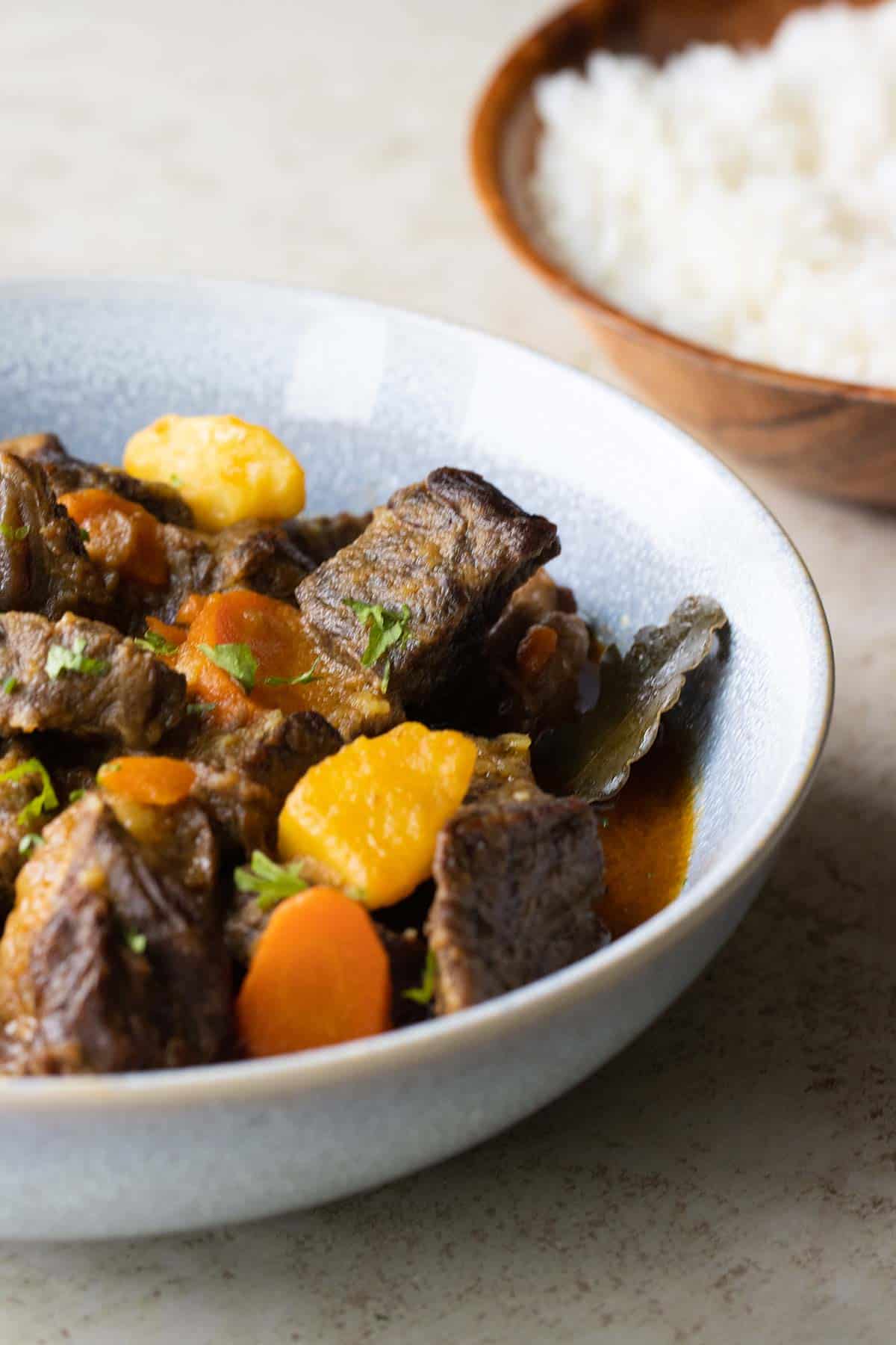 un plato azul con carne de res guisada con papas, zanahorias y una hojita de laurel.