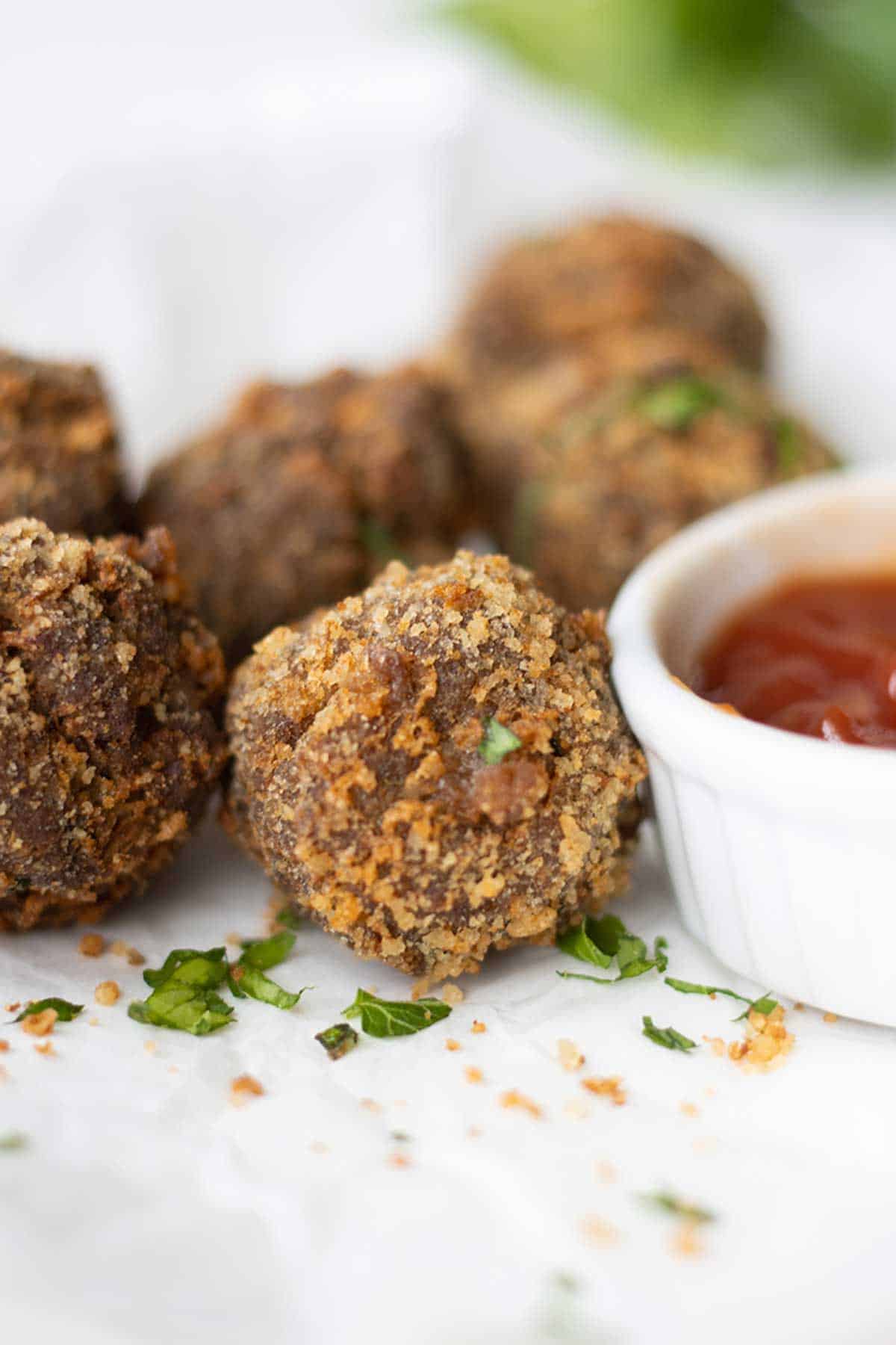 vista cercana de unas albondigas fritas con una porcion de salsa de tomate al lado.