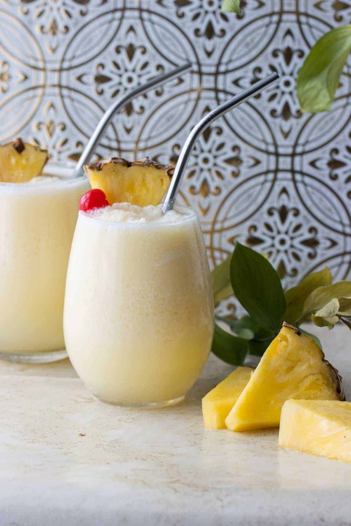 2 cups of pina colada with straws and topped with a cherry and pineapple chunks.