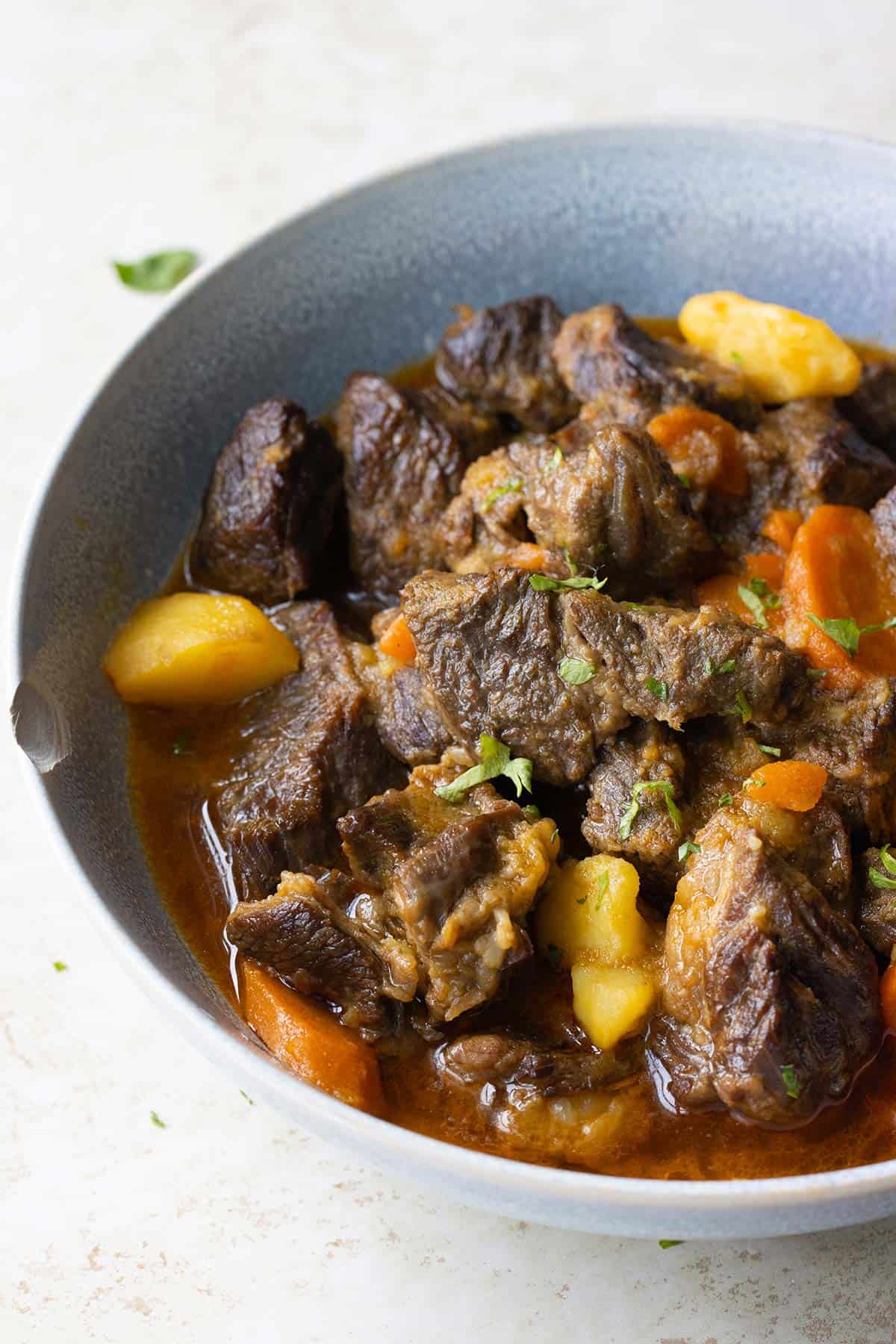 plato azul con carne guisada papas y zanahorias con perejil encima.