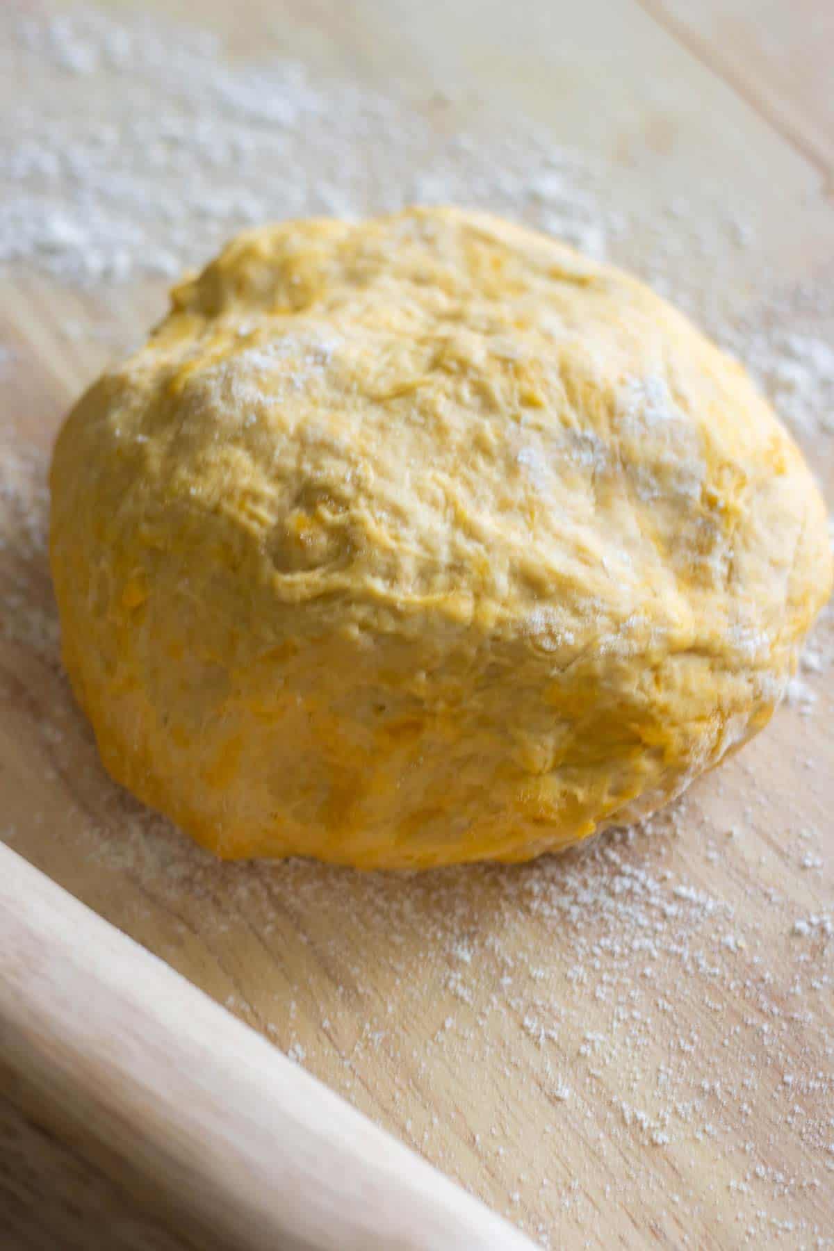 una bola grande de la masa de empanadillas sobre mesa de madera polvoreada con harina y un rodillo al lado.