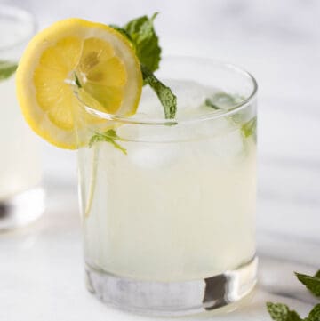 a glass with a lemon mint juice with a lemon and mint as garnish and some mint in the foreground.