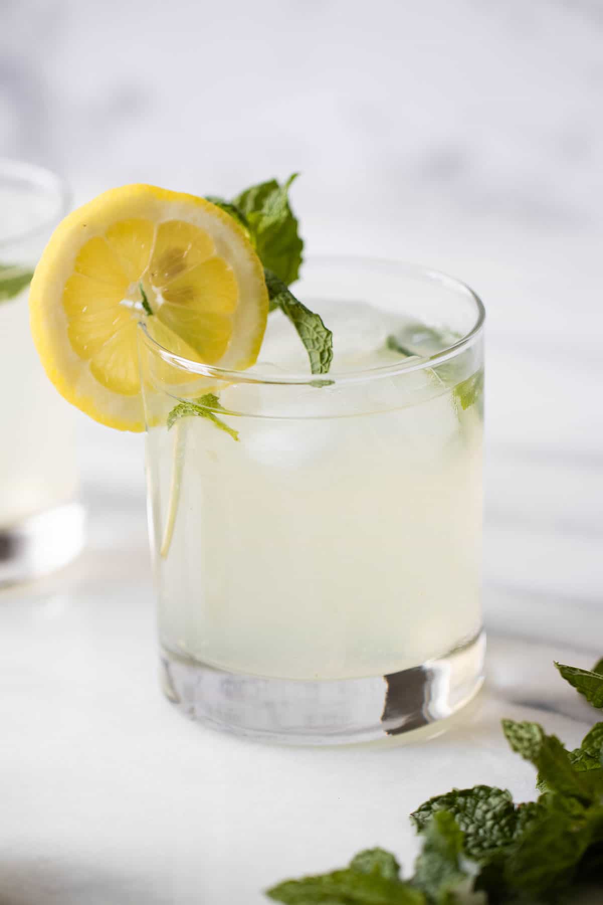 a glass with a lemon mint juice with a lemon and mint as garnish and some mint in the foreground.