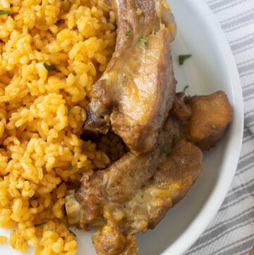 top view of a white plate with rice and pork ribs over a line pattern towel.