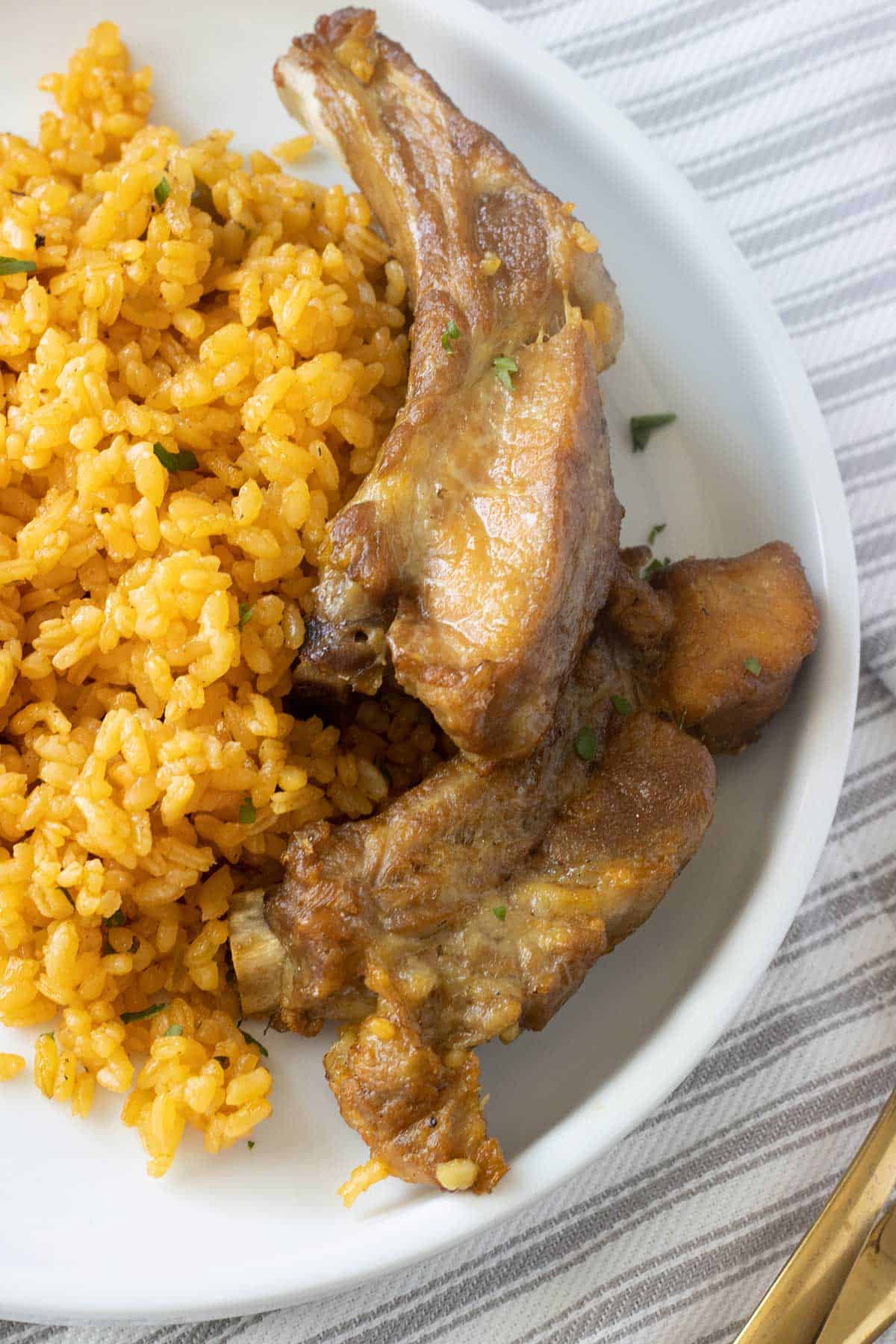 top view of a white plate with rice and pork ribs over a line pattern towel.