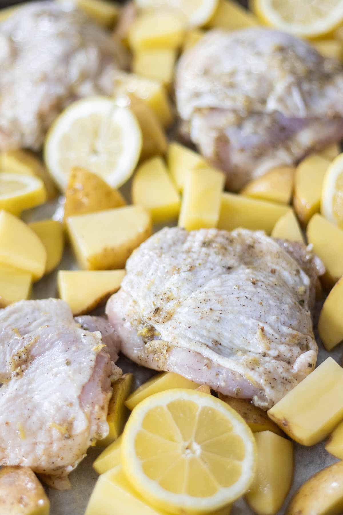various chicken thigh pieces with chopped potatoes and lemon wheels.