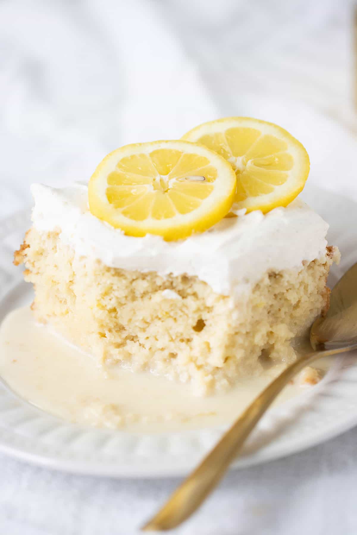 pedazo de torta tres eches de limon con una cuchara de oro sobre un plato blanco.