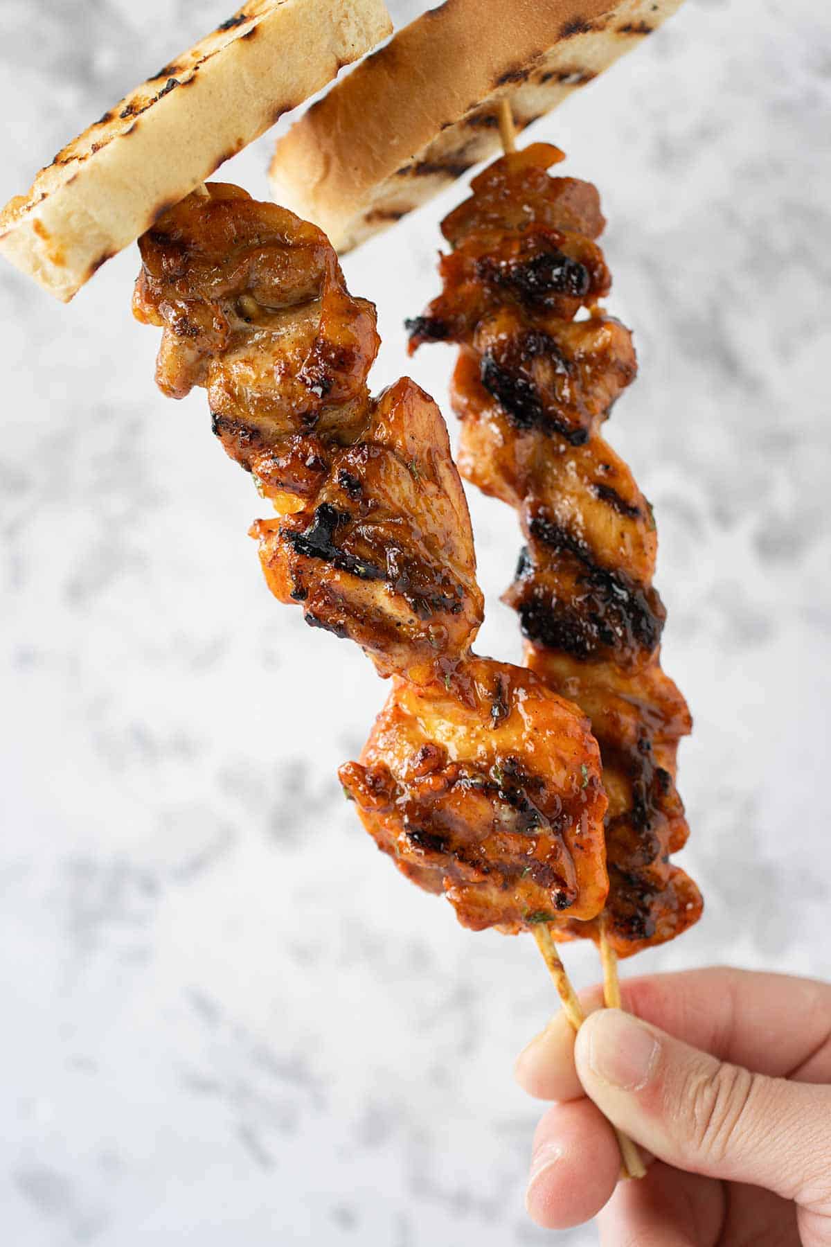 2 pinchos de pollo con salsa barbeque y un pedazo de pan sobao encima.