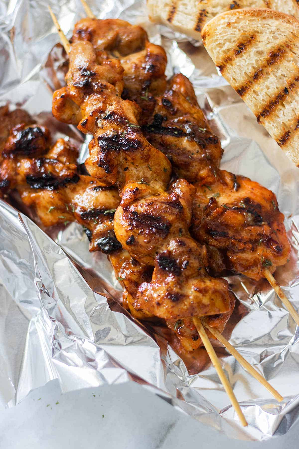3 chicken skewers with bread on foil.