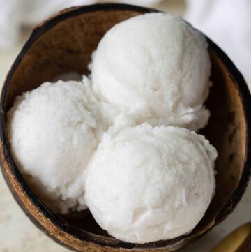 top view of 3 scoops of a coconut sorbet served on a coconut shell with a golden spoon on the side.