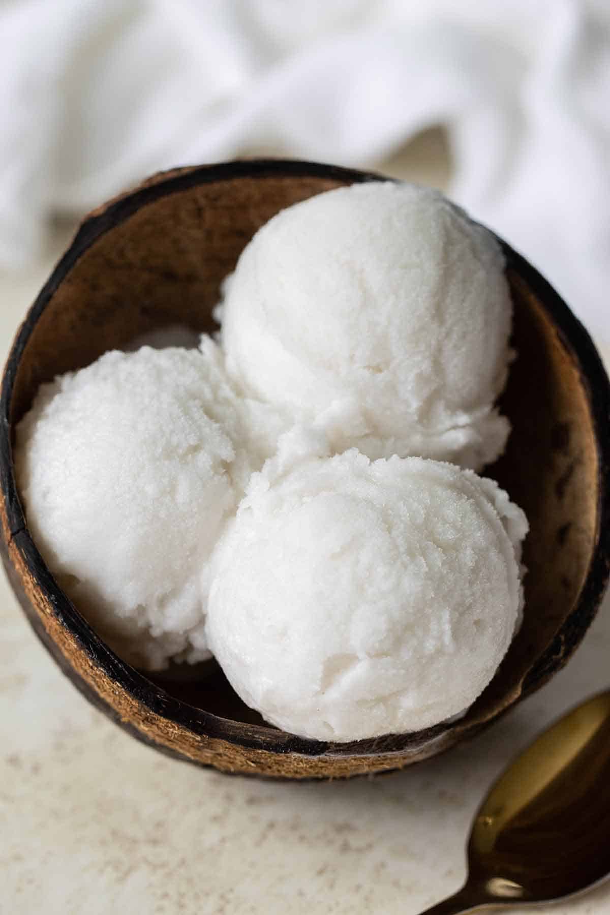 tres bolas de helado de coco dentro de un coco seco con una cuchara de oro al lado.