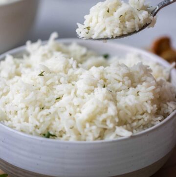 a spoonful of coconut basmati rice with a bowl of rice in the background.