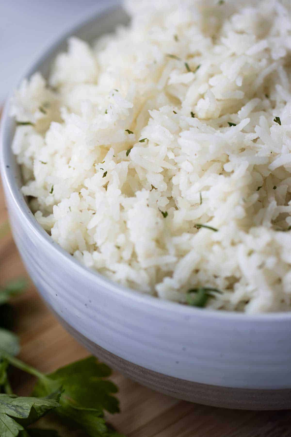 close up of a bowl full of basmati coconut rice with some parsley on the side.