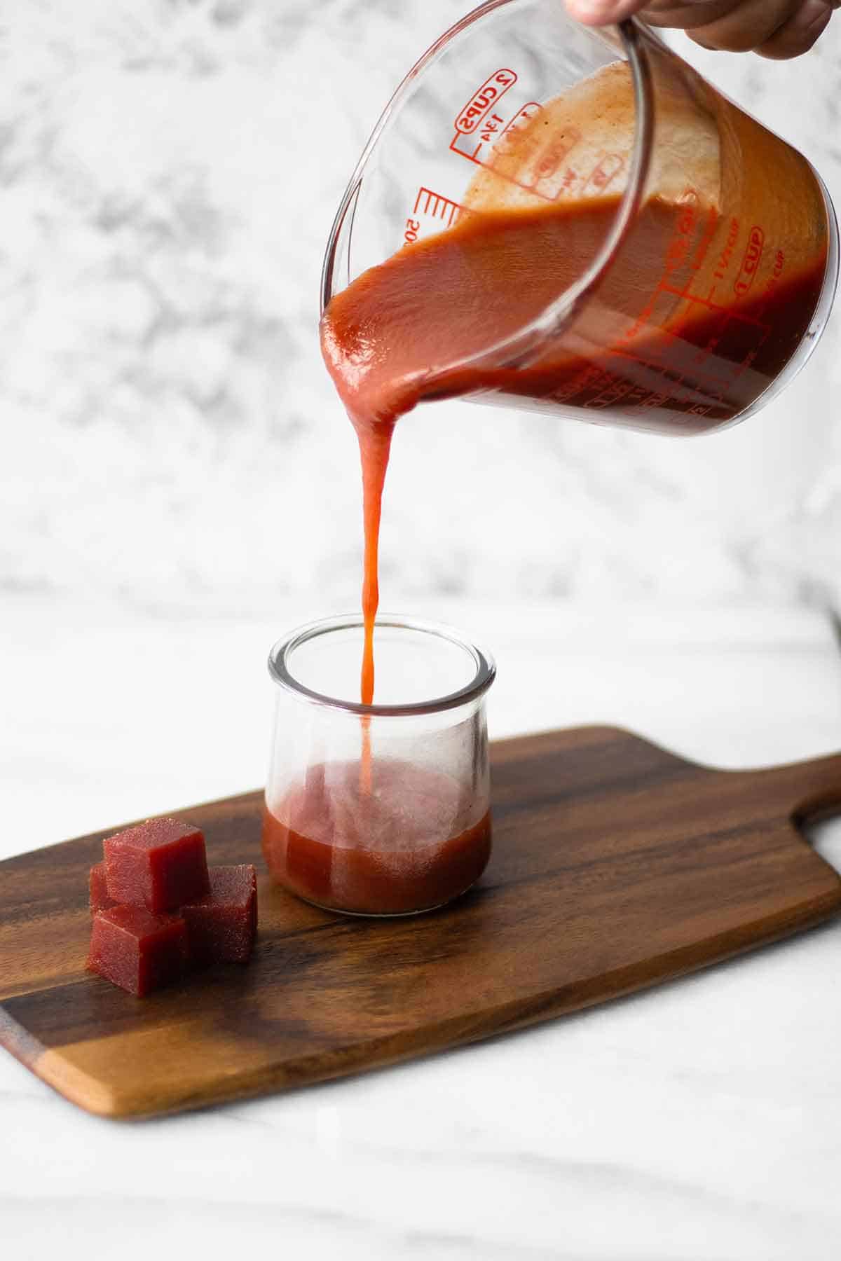mano hechando salsa de guayaba de un envase grande a un envase pequeno.