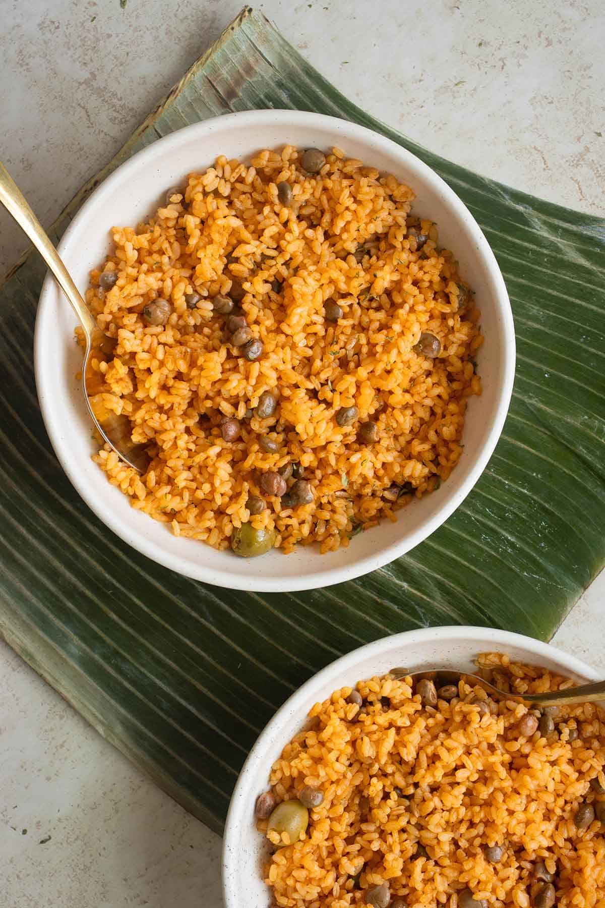 top view of 2 white bowl with arroz con gandules over a banana leaf.