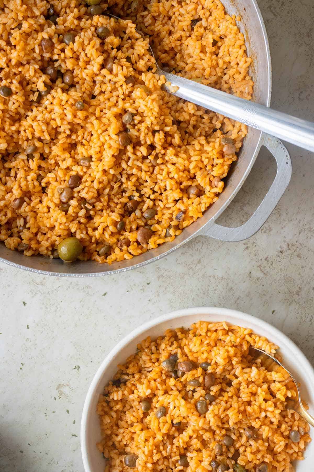 a big caldero with yellow rice and pigeon peas and a plate with rice on the side.