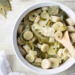 a big white bowl with guineos and escabeche and a wooden spoon with some garlic, black pepper and bay leaves as garnish.