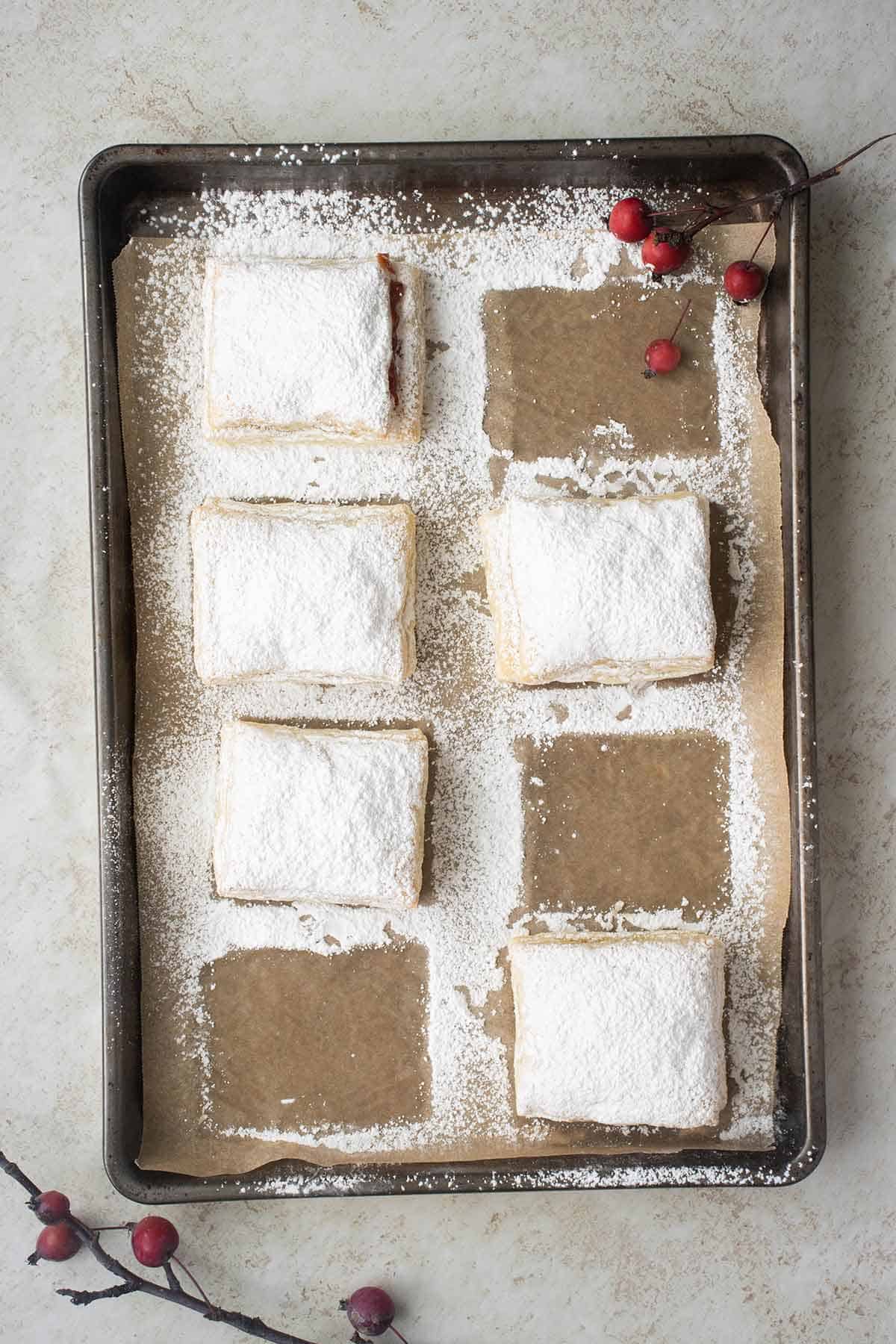a baking tray with 5 guava pastries with powder sugar and wild berries around.