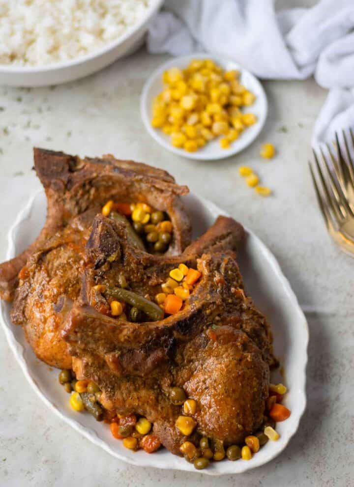 a plate with chuleta a la jardinera with a small dish with corn and a big bowl of white rice.