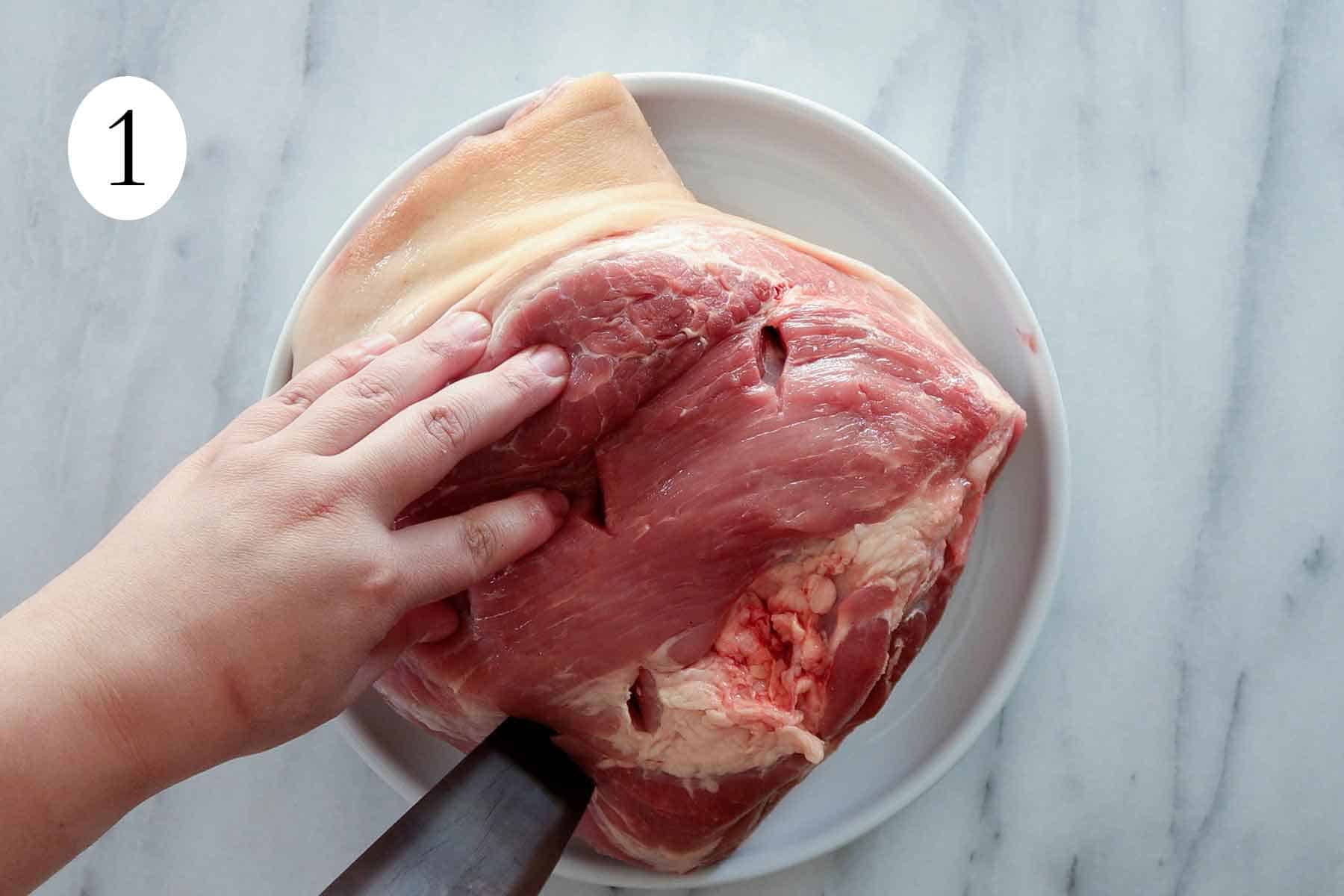 a hand making cuts to a pork shoulder.