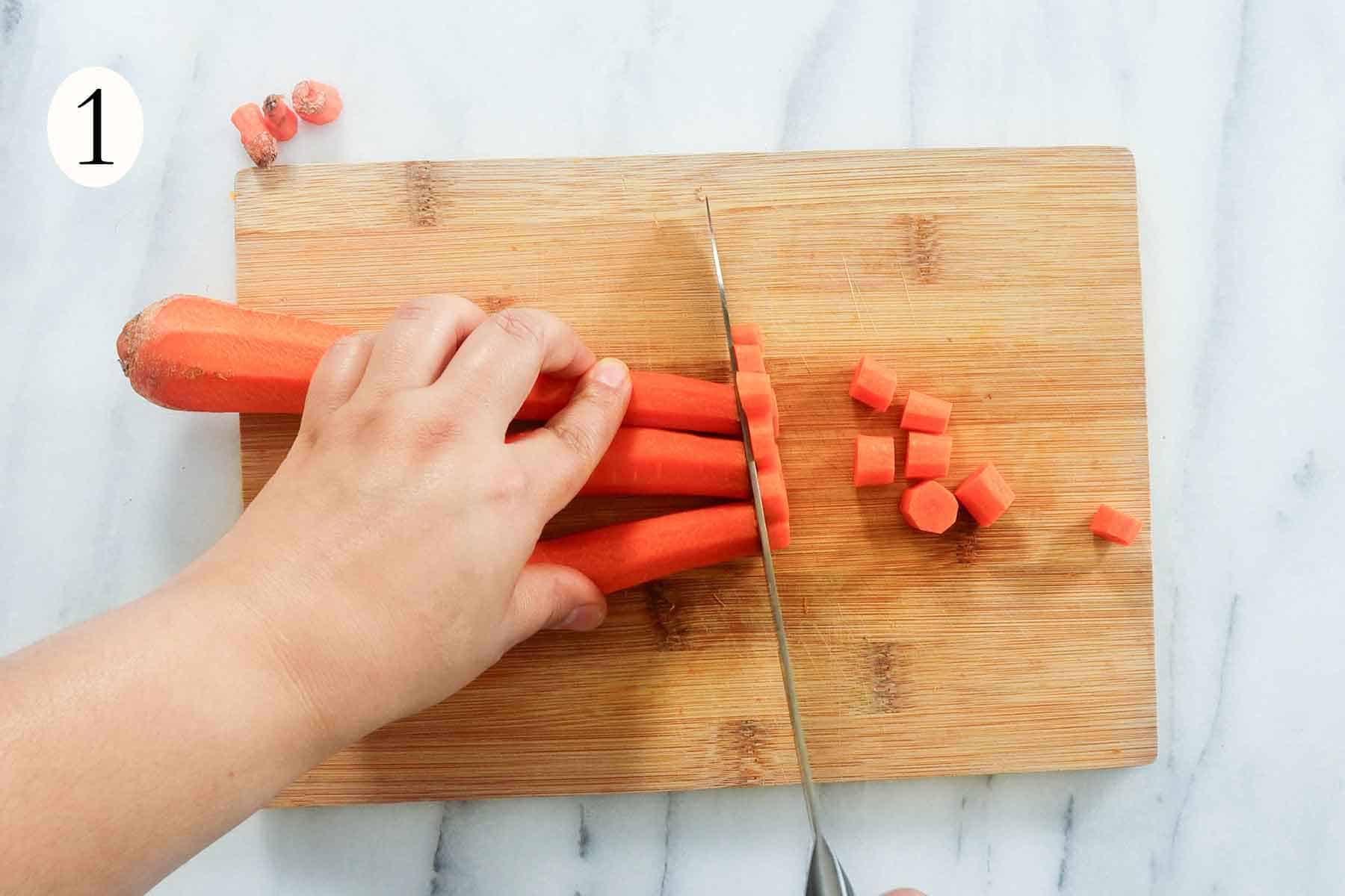 3 carrots being cut into small cylinders on a wood cutting board.