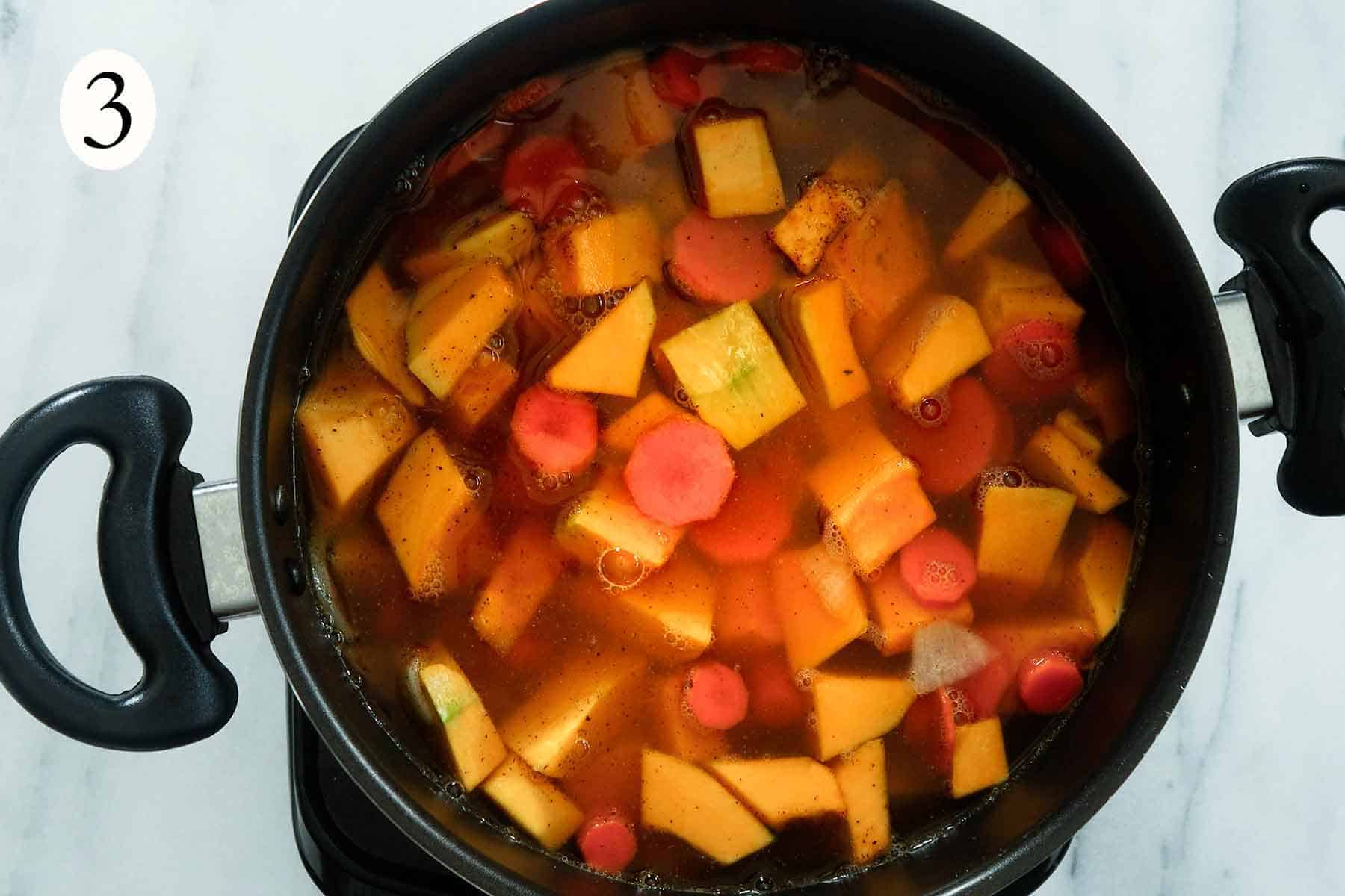 a black pot with pumpkin, carrots, onion, and stock cooking.
