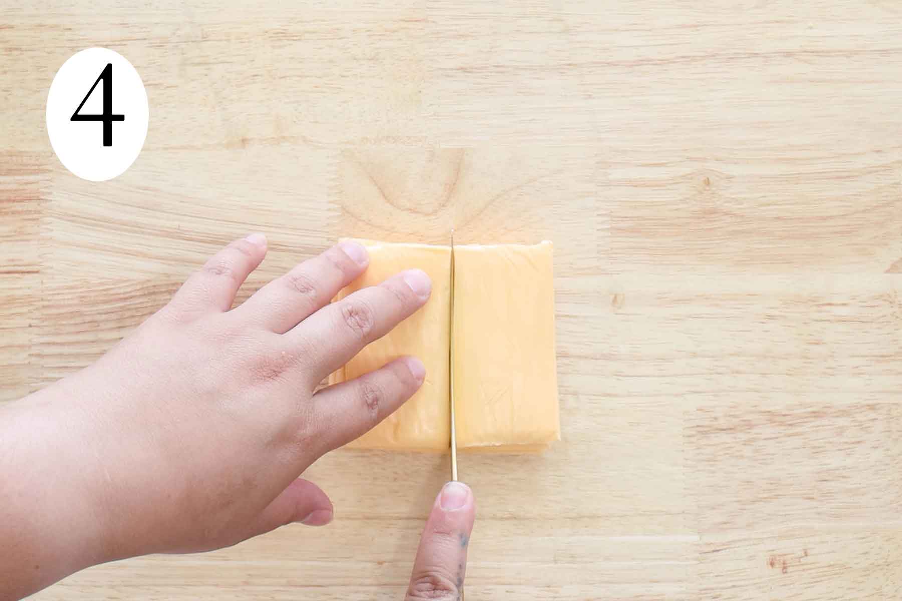 a pair of hands cutting a stack of cheese slices.