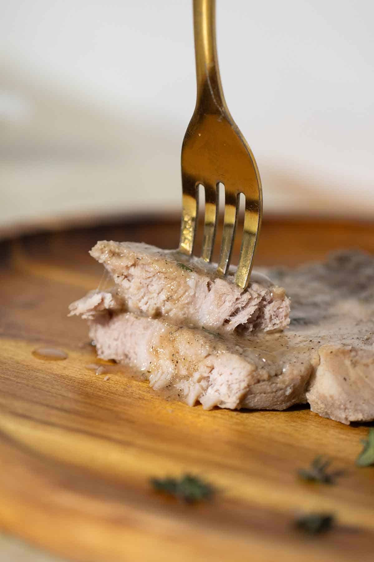 2 pieces of boiled pork chop with a fork through them.