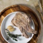 2 boiled pork chops with some garlic and fresh thyme on the side.