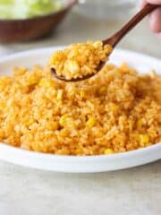 a spoonful of yellow rice with corn over a plate with rice.