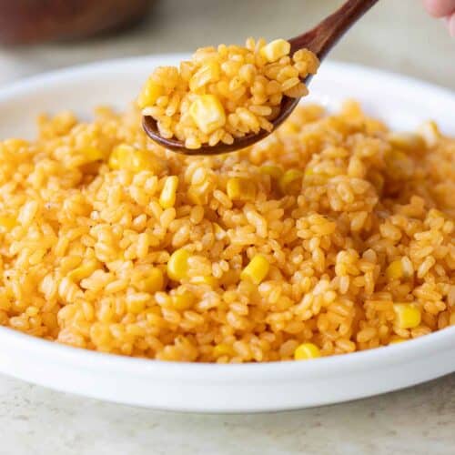 a spoonful of yellow rice with corn over a plate with rice.