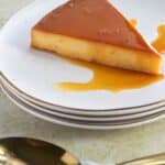 a piece of flan de parcha on a stack of plates with some spoons on the side.