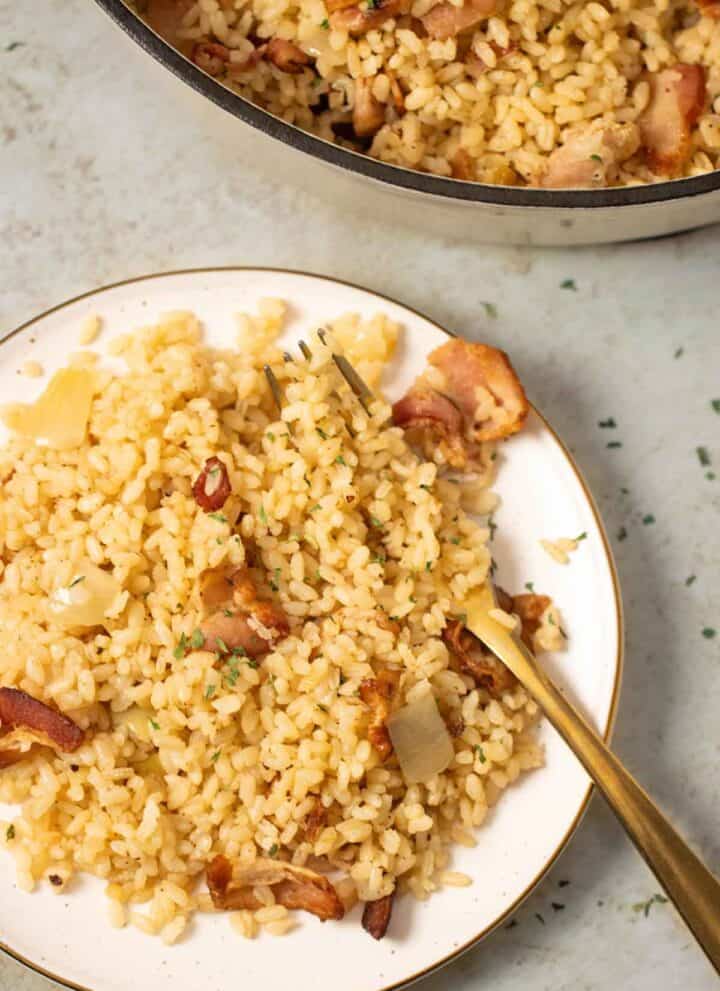 a big pot on the background and a small plate with bacon rice with onions and a fork on the side.