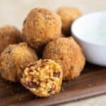 a wood plate full of puerto rican bolitas de arroz mamposteado and one rice ball open in half.