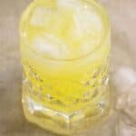 a glass cup full of a limoncillo drink with a few pieces of ice on the side.