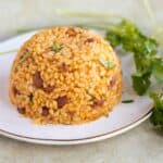 a plate with puerto rican arroz mamposteado in a dome shape with cilantro on the side.