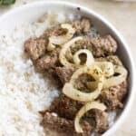 a plate with white rice and a puerto rican style bistec encebollado.