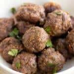 a white balls with lots of baked meatballs garnished with parsley.