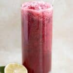 a cup full of a berry lemonade with a few blueberries on the side and half of lime.