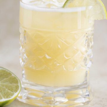 a cup of pineapple lemonade with a piece of lime on the side.