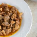 a plate of carne de cerdo guisada with a pot of meat in the back.