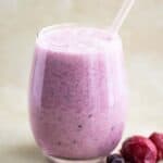 a cup with a coconut and berries smoothie with a couple of berries on the side.